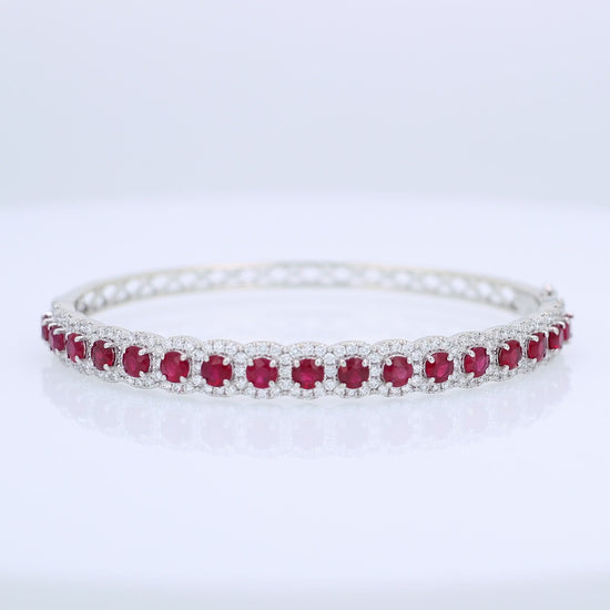 White gold bangle bracelet with red rubies and diamond halo accents on a white background