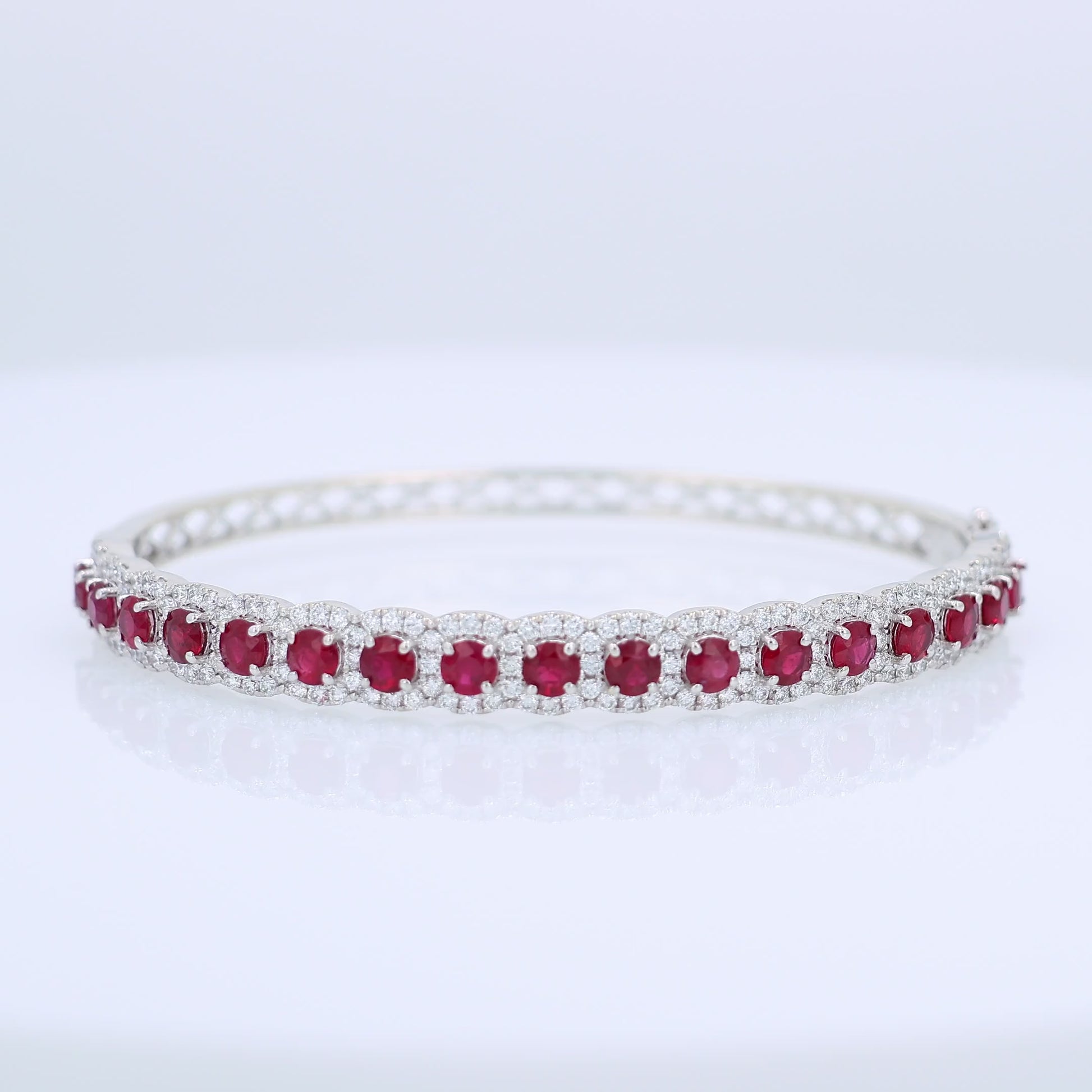 White gold bangle bracelet with red rubies and diamond halo accents on a white background