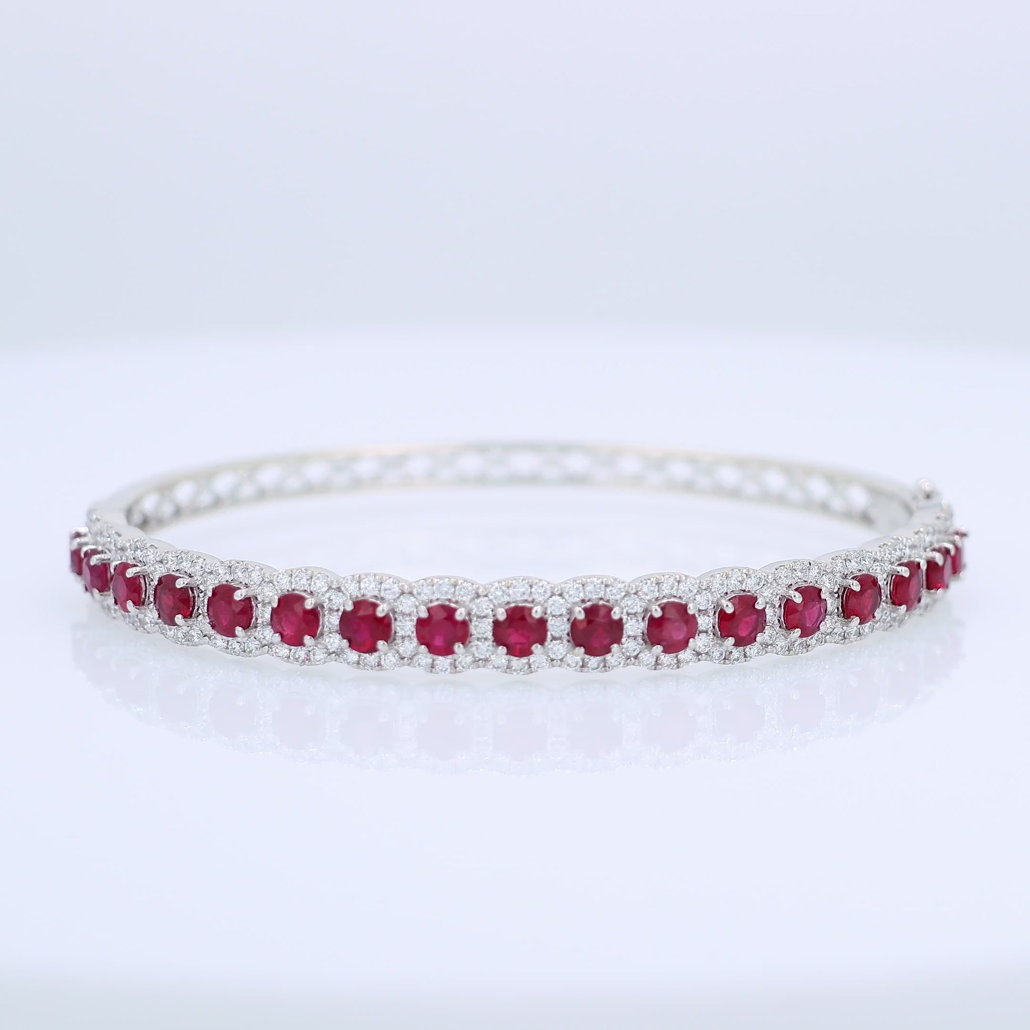 White gold bangle bracelet with red rubies and diamond halo accents on a white background