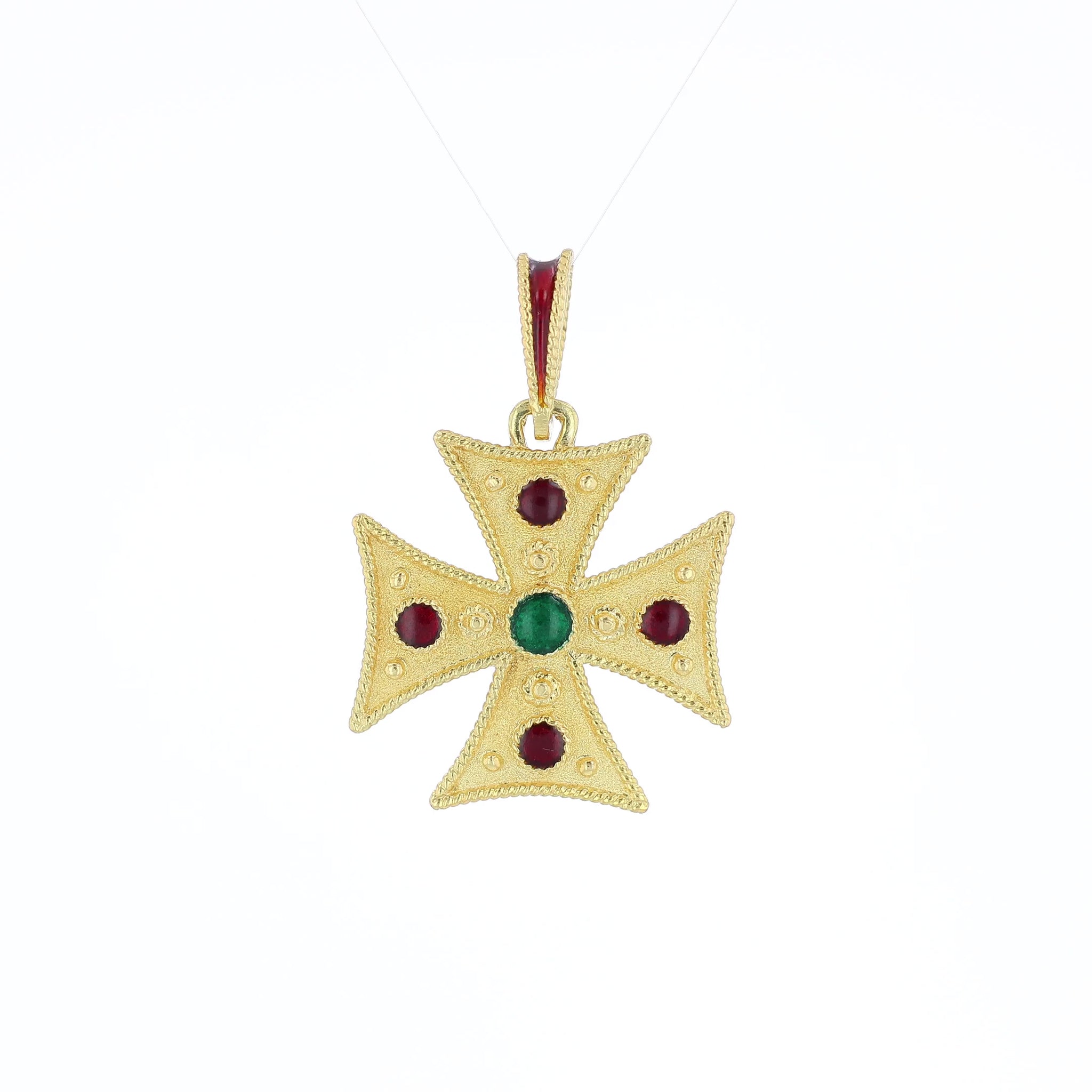 Yellow gold textured cross pendant with red and green glass accents on the face and red enamel on the bail on a white background