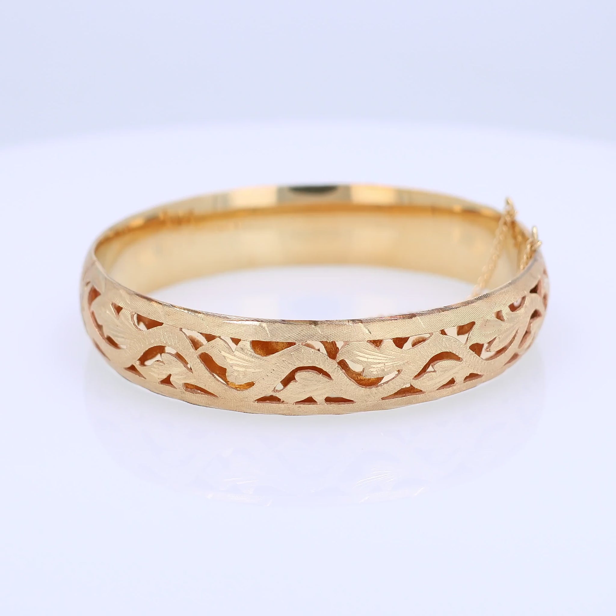 Yellow gold brushed open work design bangle bracelet on a white background