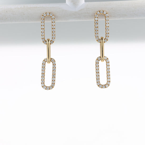 A video of a pair of gold drop earrings with elongated oval links, each pavé-set with clear stones, shown on a off white bar and at various angles on a clean white background with a soft reflection below.