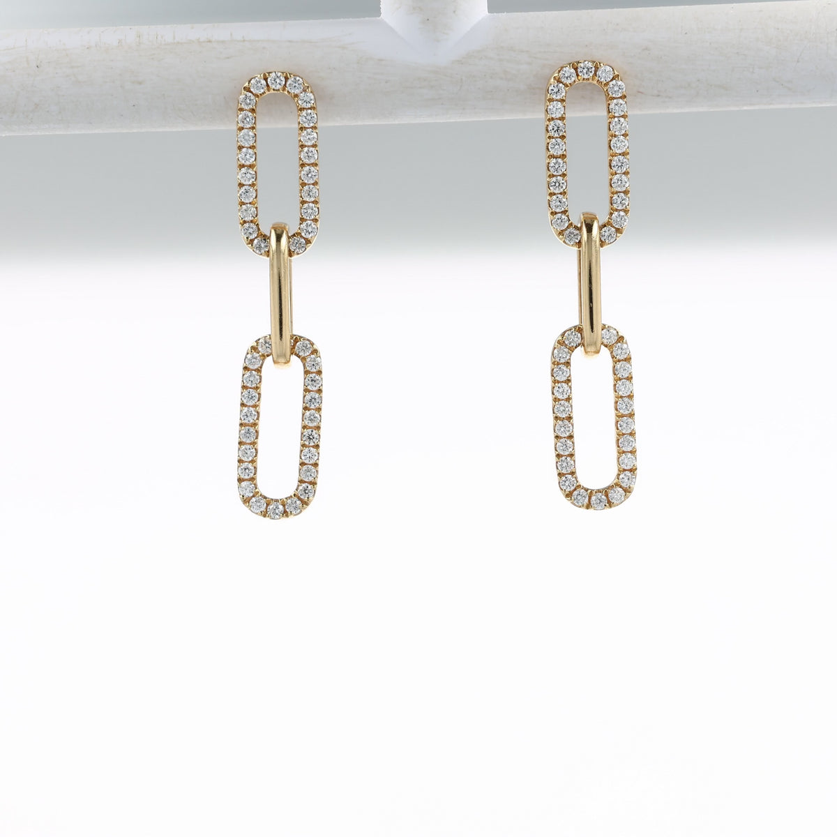 A video of a pair of gold drop earrings with elongated oval links, each pavé-set with clear stones, shown on a off white bar and at various angles on a clean white background with a soft reflection below.