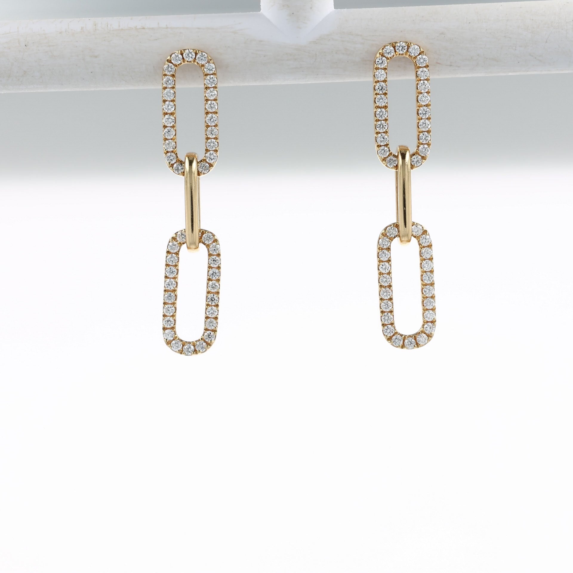 A video of a pair of gold drop earrings with elongated oval links, each pavé-set with clear stones, shown on a off white bar and at various angles on a clean white background with a soft reflection below.