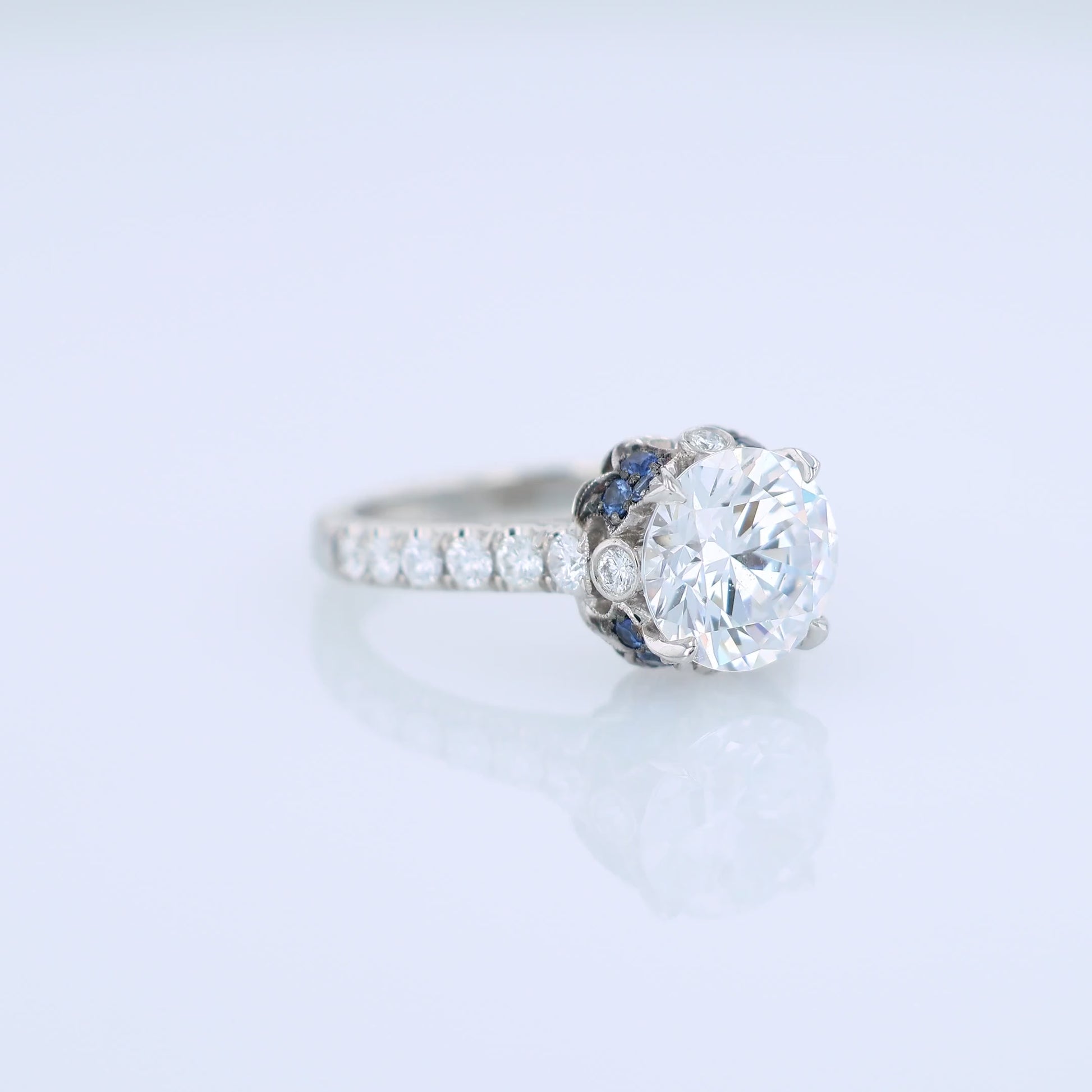 Platinum diamond engagement ring with diamond and sapphire accents and a round cubic zirconia center on a white background