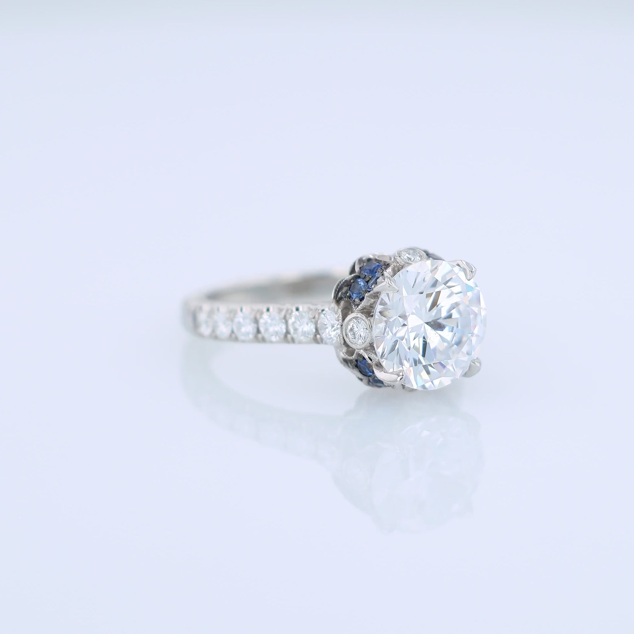 Platinum diamond engagement ring with diamond and sapphire accents and a round cubic zirconia center on a white background