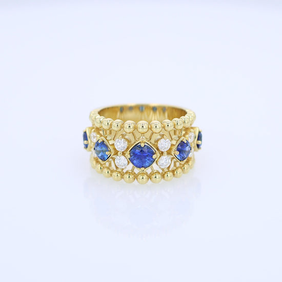 Yellow gold open work ring with diamond and blue sapphire accents on a white background
