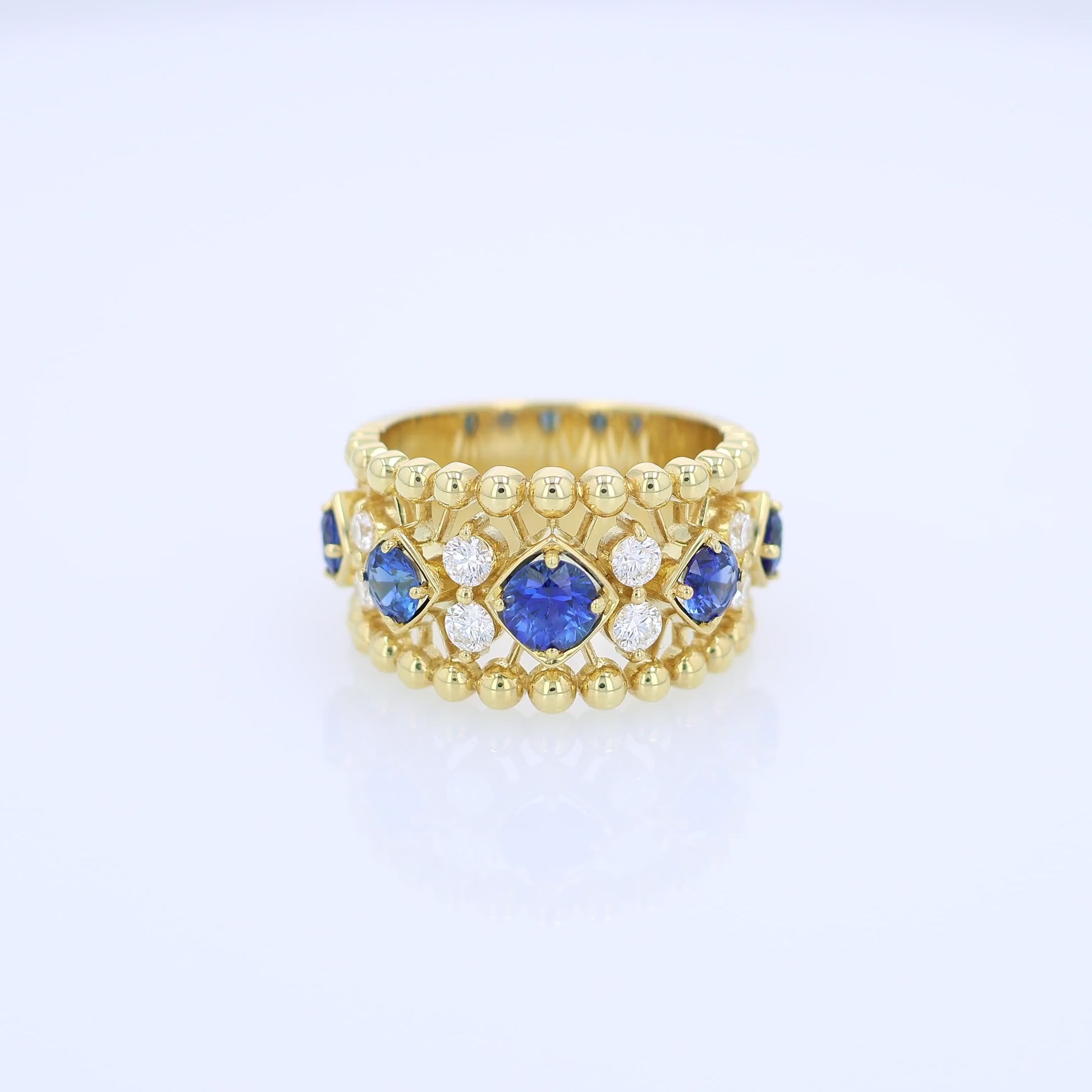 Yellow gold open work ring with diamond and blue sapphire accents on a white background