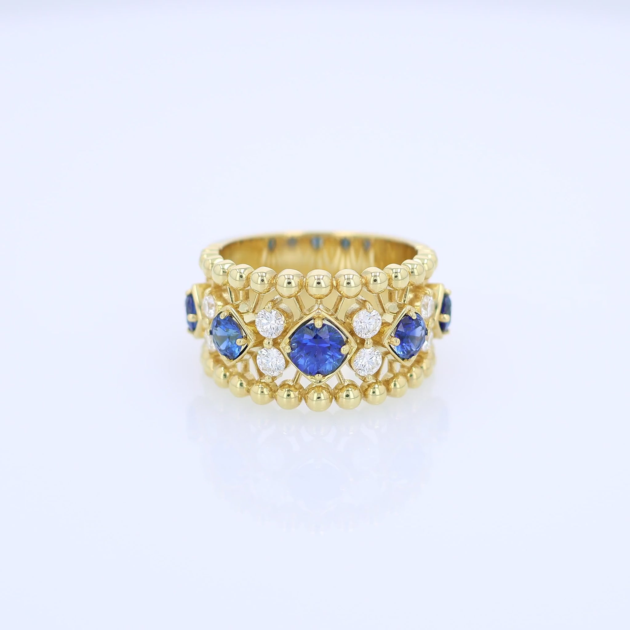 Yellow gold open work ring with diamond and blue sapphire accents on a white background