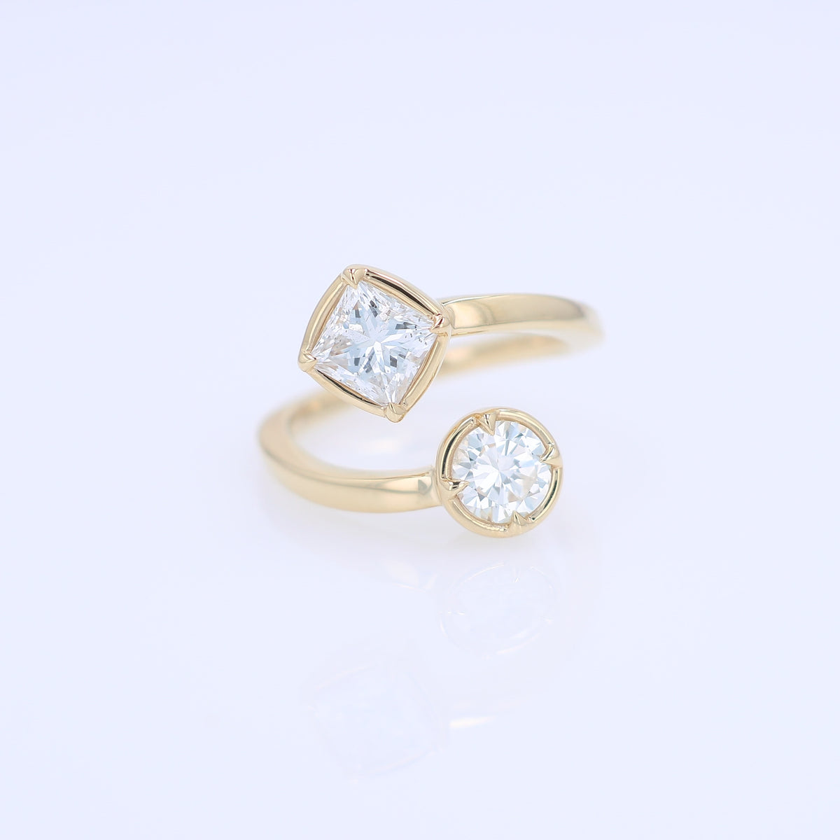 A yellow gold bypass ring featuring diamonds - a princess-cut and a round brilliant-cut diamond - on a clean white background.