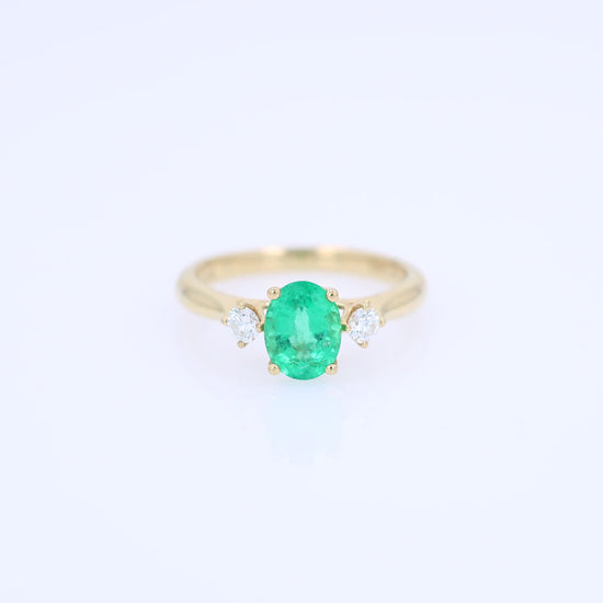 Gold ring with an oval emerald center and diamond sides on a white background