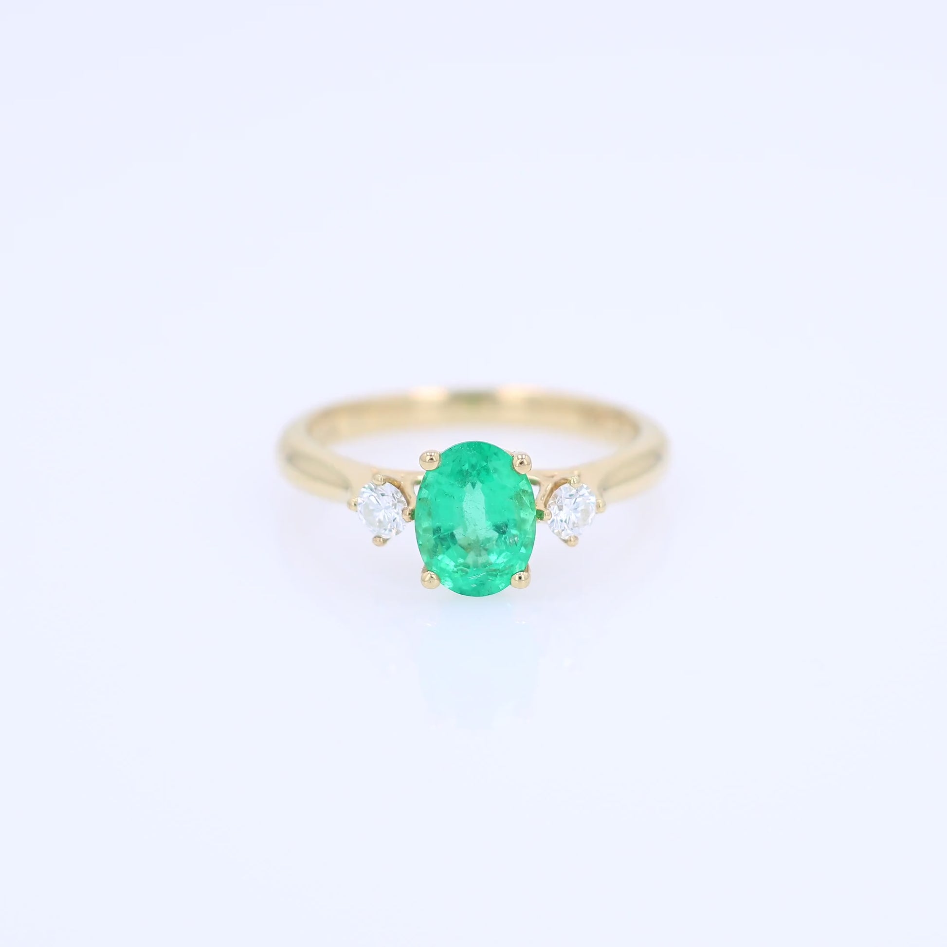 Gold ring with an oval emerald center and diamond sides on a white background