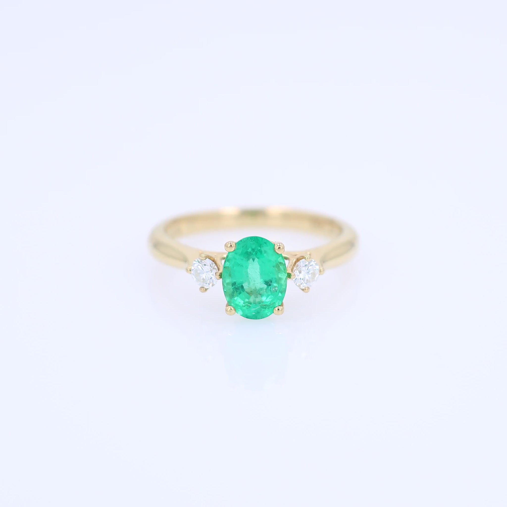 Gold ring with an oval emerald center and diamond sides on a white background