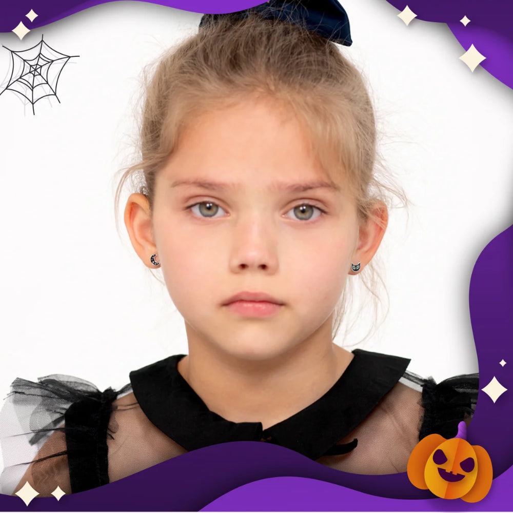 A young girl with blonde hair in a high bun wearing a black tulle top with a ruffled collar, shown against a white background with purple Halloween-themed graphic borders and spiderwebs.