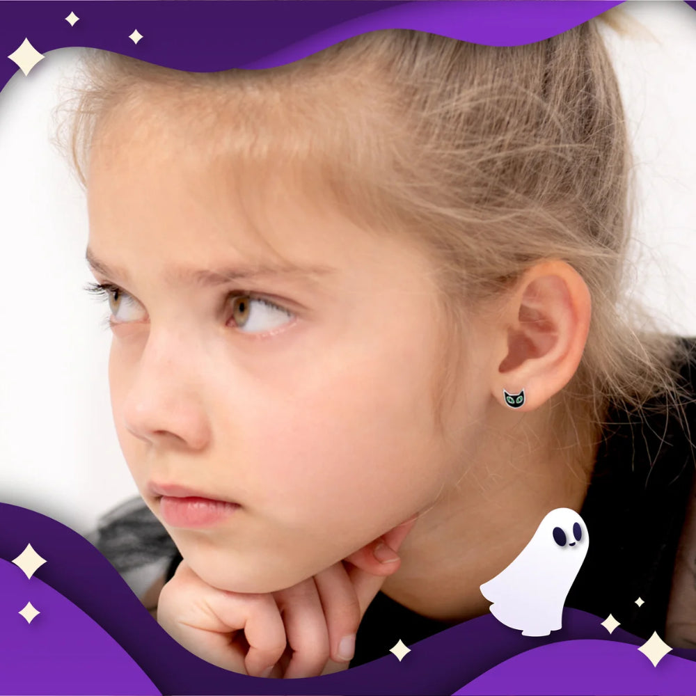 A close-up of a young girl with blonde hair in a ponytail, wearing a small black cat-shaped stud earring. The image has a stylized purple Halloween-themed border with stars and a white ghost graphic.