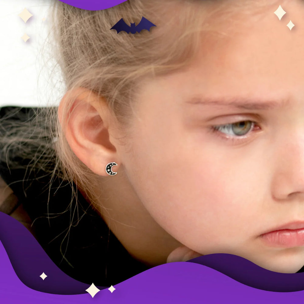 A close-up of a young girl wearing a small crescent moon stud earring with a black and white pattern and a tiny pink accent. The image features decorative purple graphic overlays at the bottom and top.