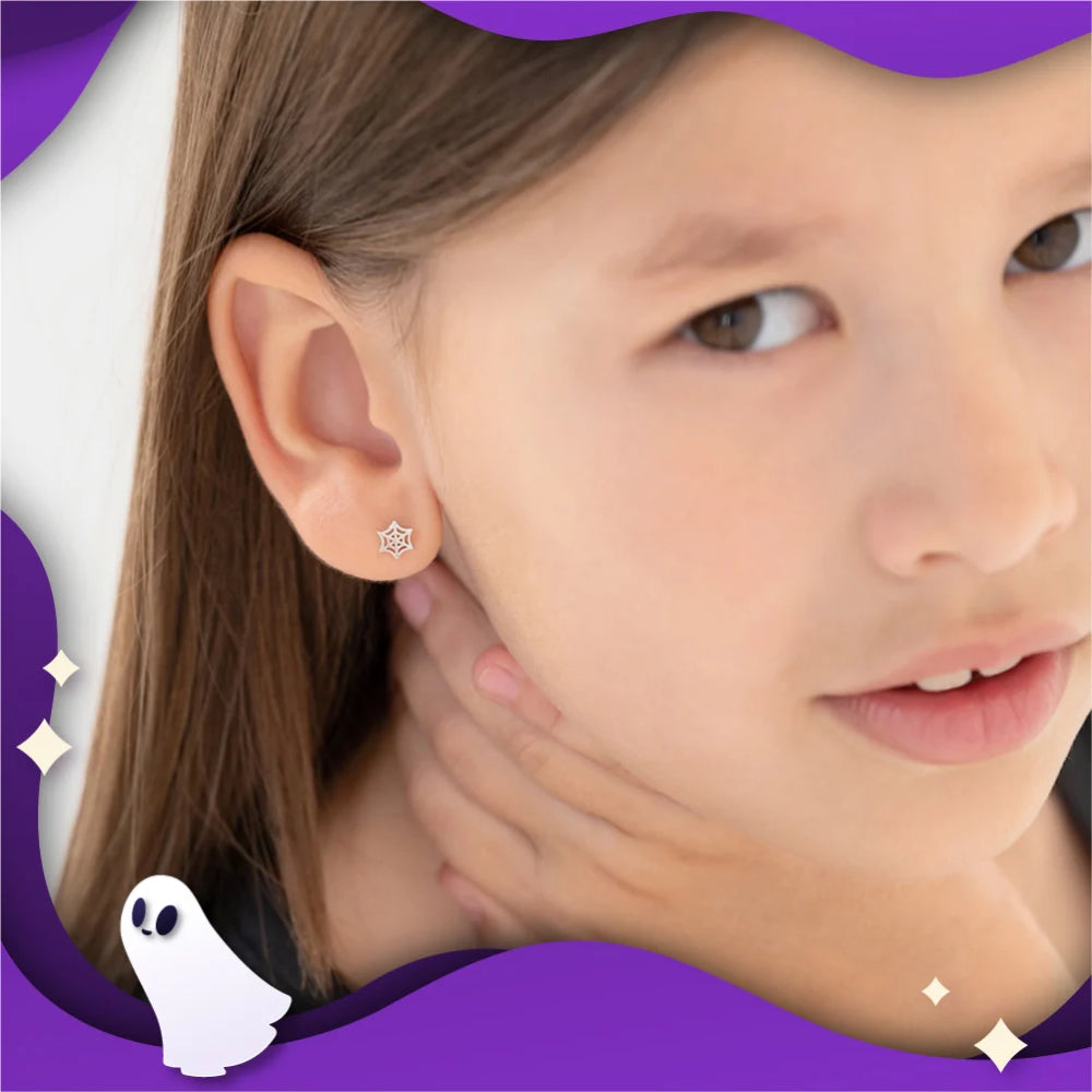 A close-up of a young girl wearing a small silver spider earring, with decorative purple graphic borders and a small ghost illustration around the edges.