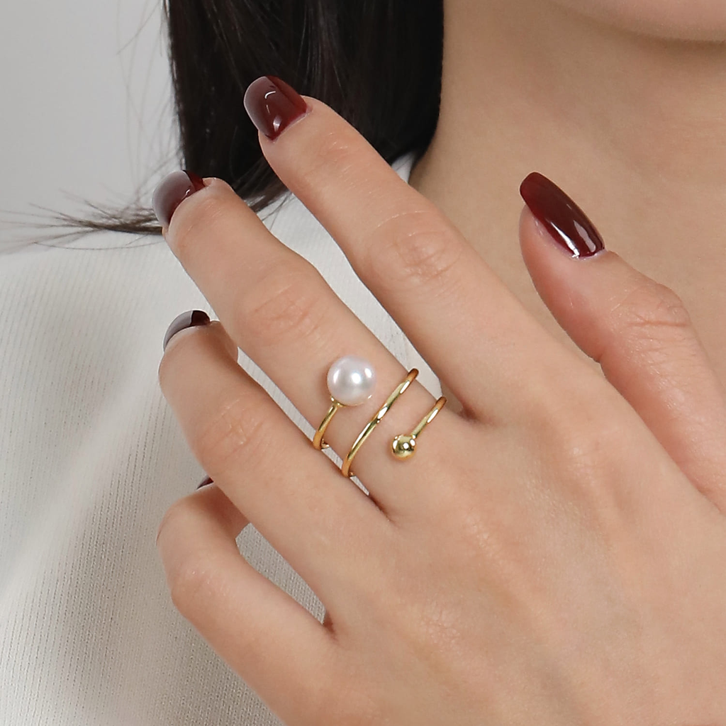 Close-up of a hand wearing gold rings with pearls on a neutral background