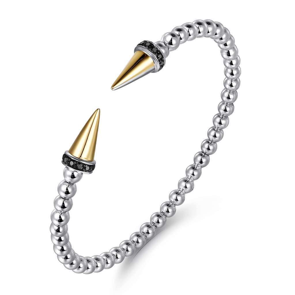 Silver beaded bracelet with gold and black spike ends on a white background