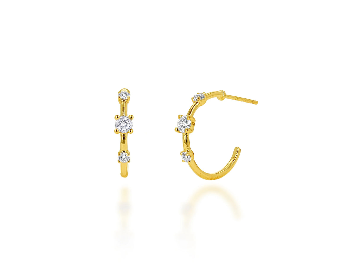 A pair of gold huggie hoop earrings with small clear gemstones, shown on a clean white background with a soft reflection.