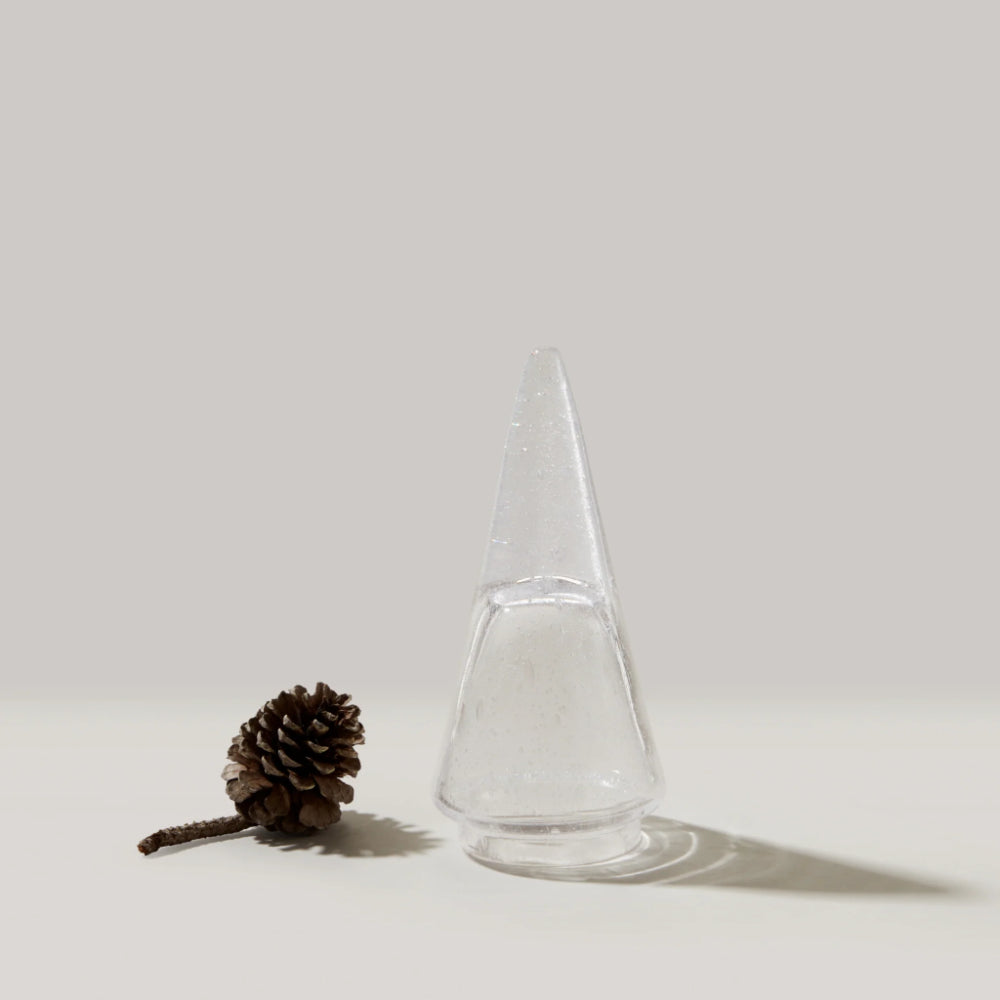 Clear glass cone-shaped object next to a pine cone on a white background