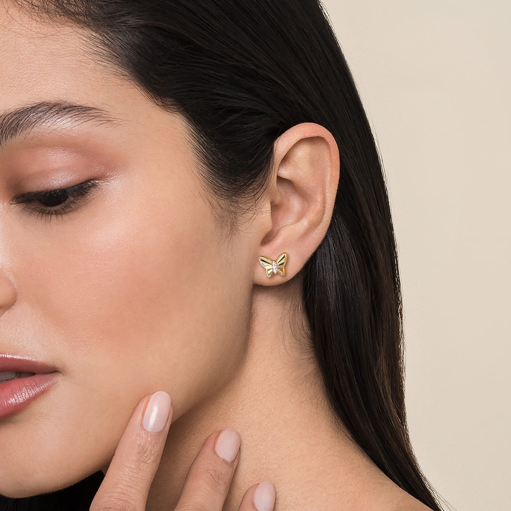Close-up of a woman wearing a gold butterfly earring on a beige background