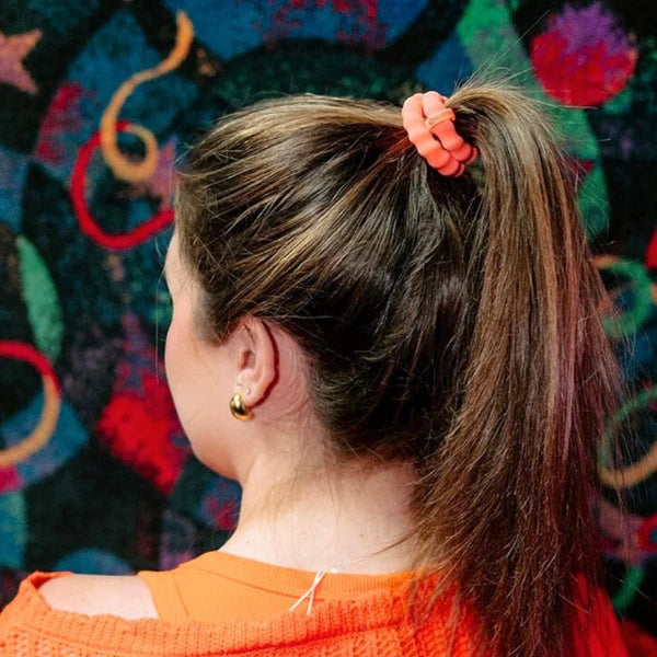Person with a ponytail wearing an orange hair tie in front of a colorful abstract background