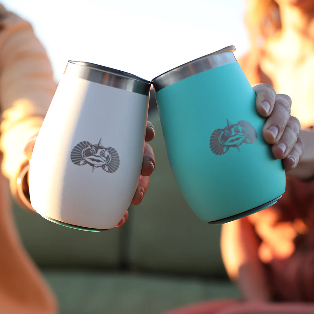 Two people are holding silver and teal Toadfish 10oz Non-Tipping Wine Tumblers, clinking them together.