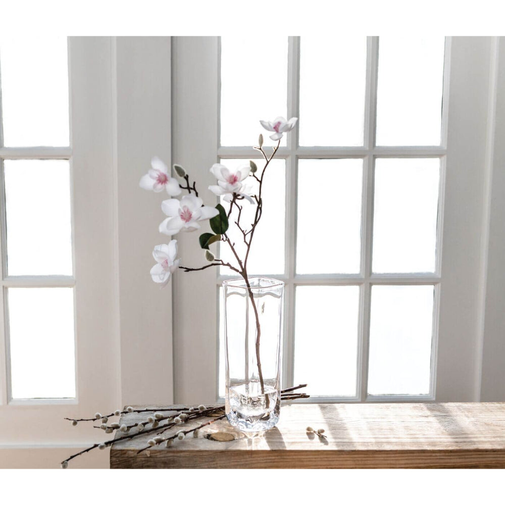 Clear glass vase on a white windowed background with white flowers in it on a wood table