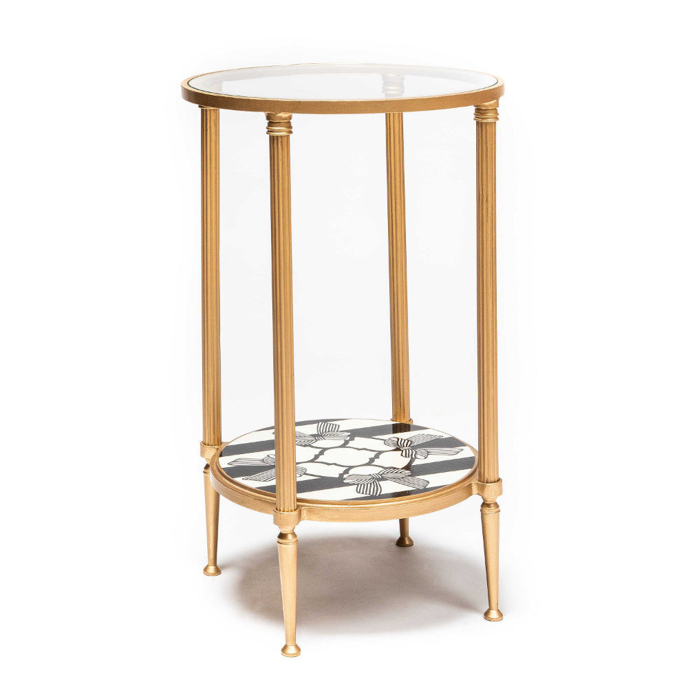 Gold-framed glass side table with a decorative white and black lower shelf on a white background