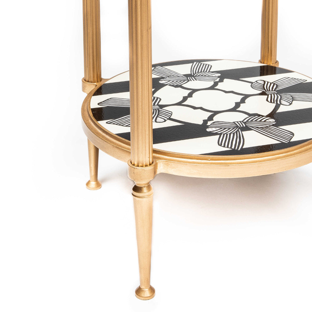 A close up photo of the bottom of a gold-framed glass side table with a decorative white and black lower shelf on a white background
