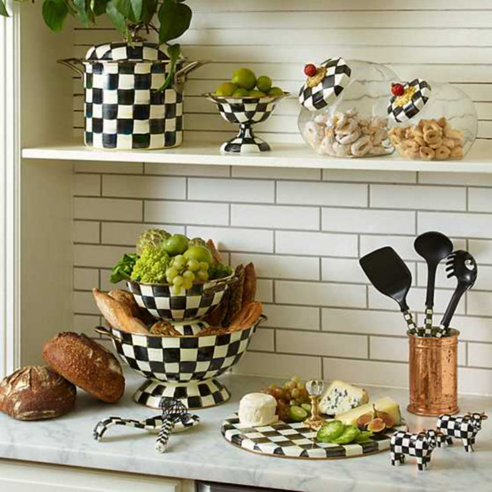 Kitchen counter with checkered bowls, fruits, bread, and utensils against a tiled white wall. 