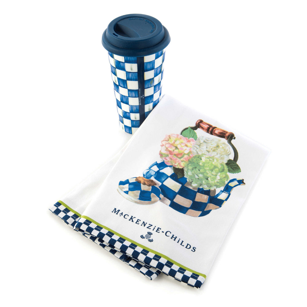 White towel with a royal check floral teapot design and 'Mackenzie-Childs' branding and royal check cup with blue top on a white backround. 