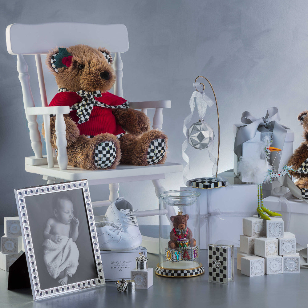 Two silver containers with black & white checkered tops and silver duck topings with yellow beeks. Labeled 'First Tooth' and 'First Curl' with other baby shower decor on a grey table with grey backround. 