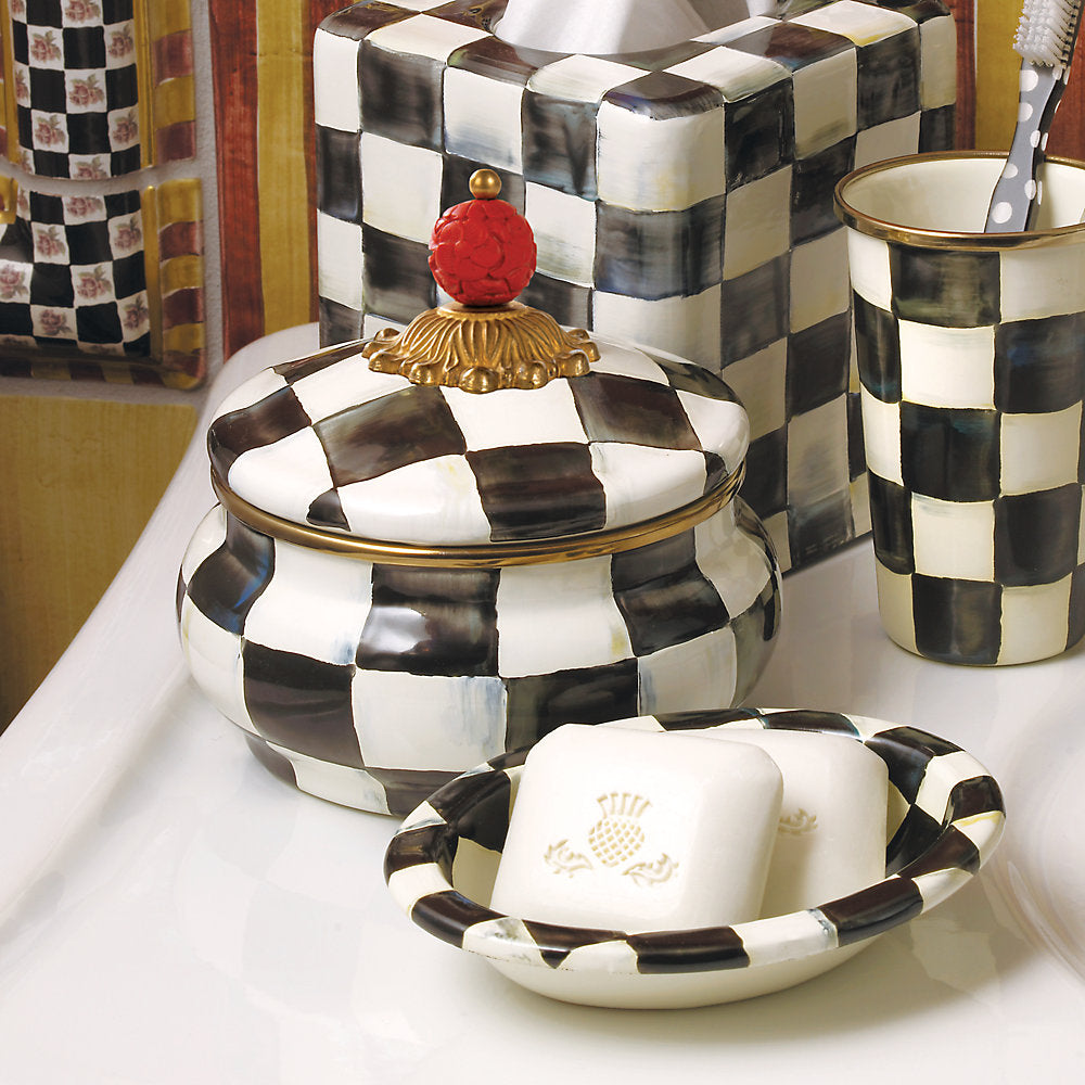 Life style photo of a decorative jar with black checkered pattern and ornate lid on a white counter top with other checkard items in the background.