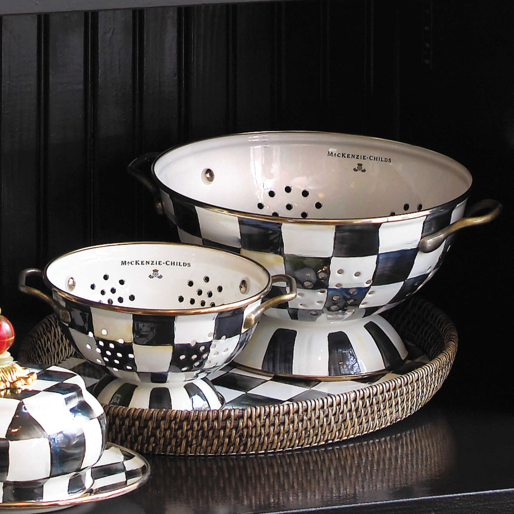 Two Decorative colander with checkered black & white pattern and gold accents on a tray that is on a black shelf. 