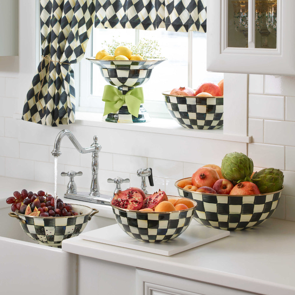 Black & White Checkered colander with gold handles in a sink in a white painted kitchen with other simular items. 