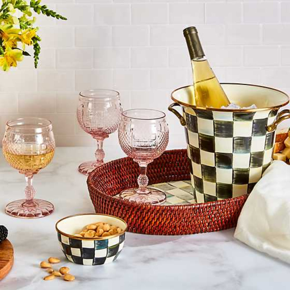 Life style photo of a small round woven tray with a brown rim on a sterling grey checkered patterned bottom on a table with other drink glasses and items. 
