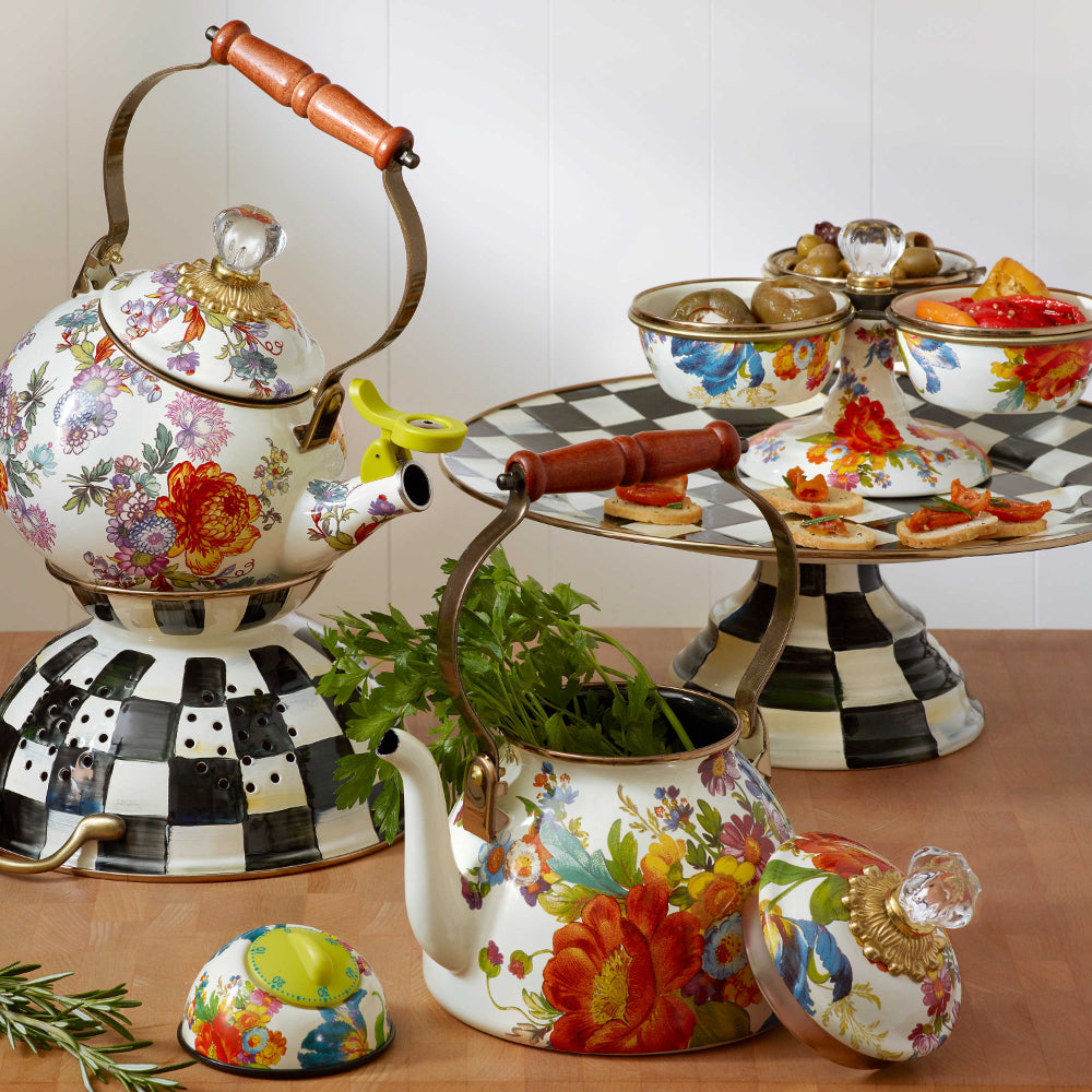 Decorative white teapot with colorful floral patterns with other Mackenzie-Childs courtly check and flower market items on a brown table