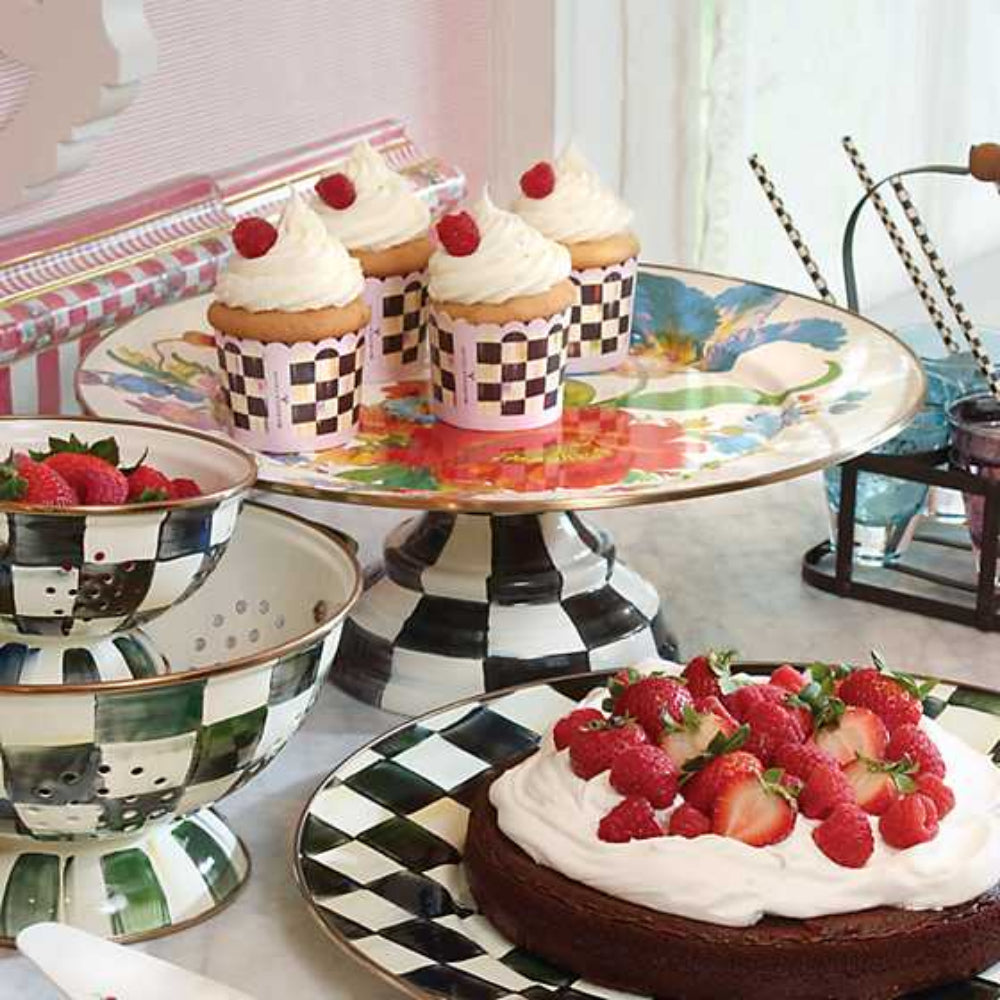 Decorative table setting with cupcakes, a cake, and bowls of raspberries on a and white black checkered stand.