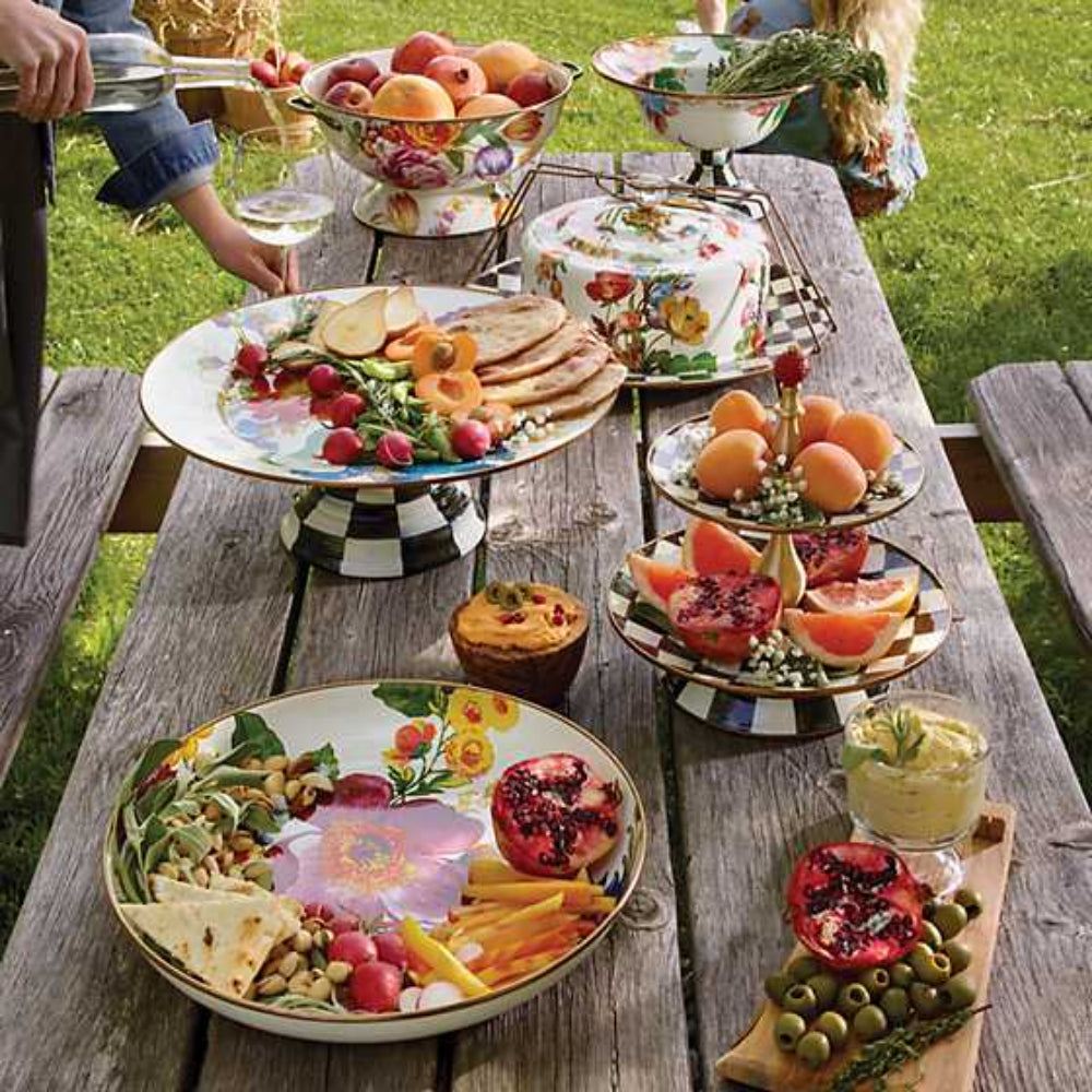 MacKenzie-Childs flower market white enamel large pedestal platter on a outside picknick table with other mackenzie items. 