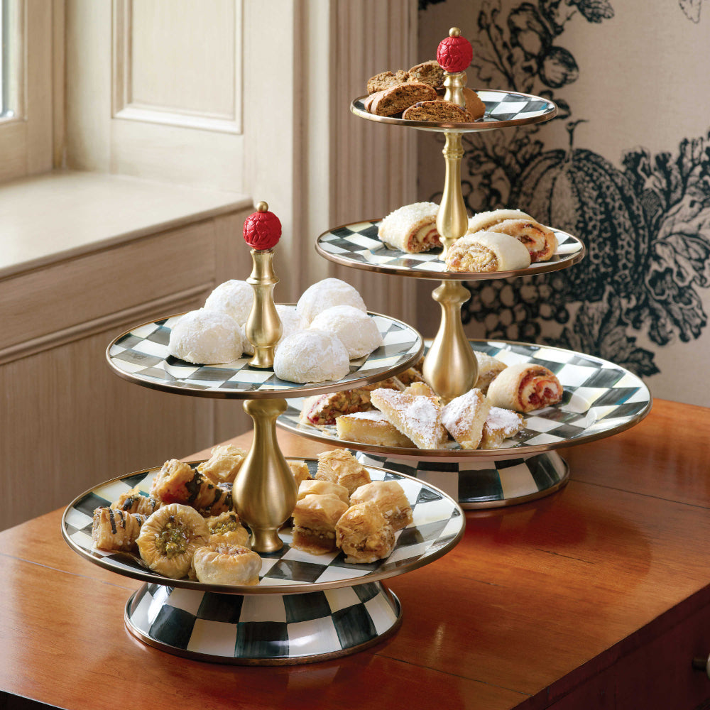 Two two-tiered serving tray with black and white checkered design and gold accents on a brown table with multi-colored refreshments on them 