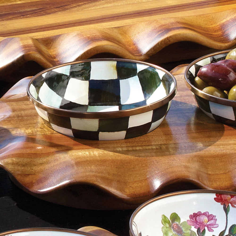 A hand-painted enameled steel relish dish with black and white checkered pattern and bronzed stainless steel rim on a ornite wood table