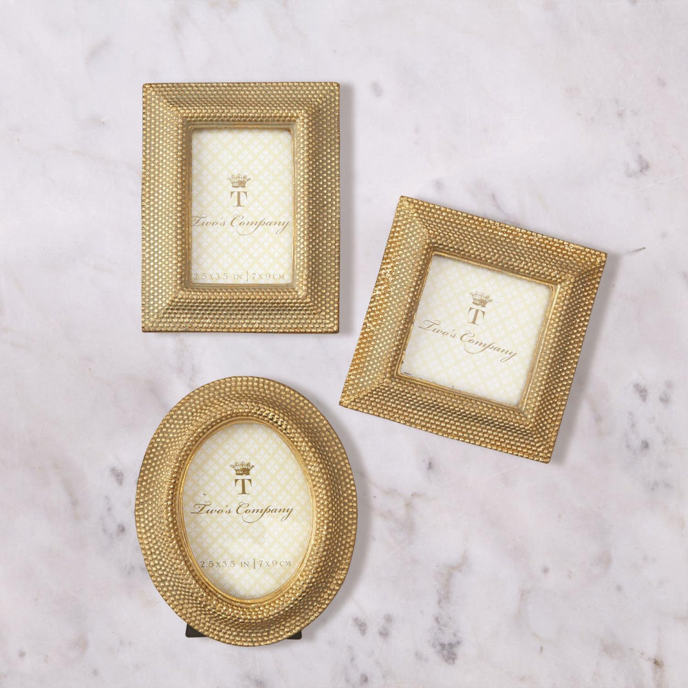 Three gold photo frames and three shapes, oval,rectangle & square  with 'TWO'S COMPANY' branding on a white marble background.