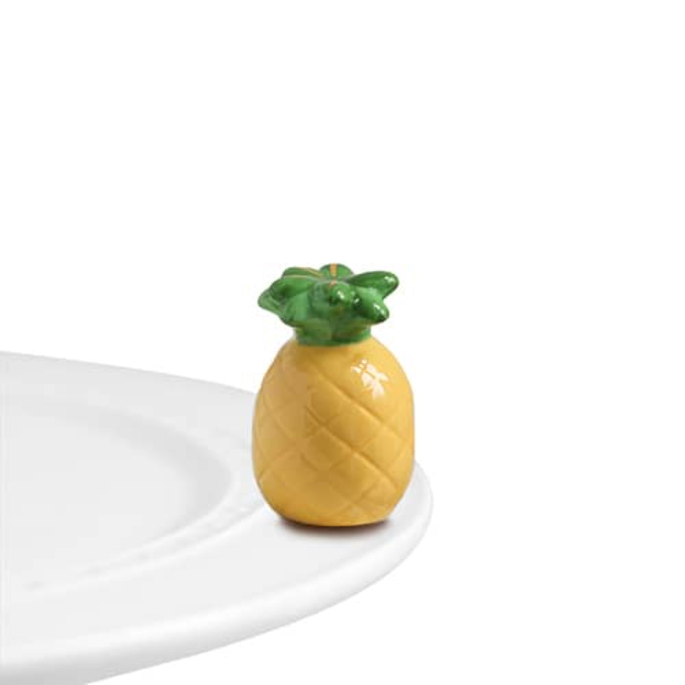 Pineapple-shaped mini decor on a white plate egde surface on a white backround 