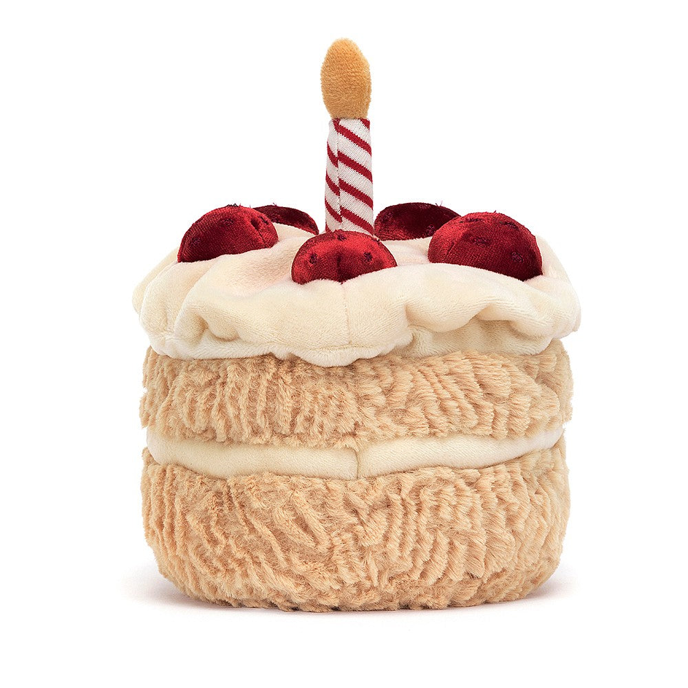 A photo of the back plush toy resembling a birthday cake with two layers, decorated with a red and white striped candle on top, and sliced pieces on the side.