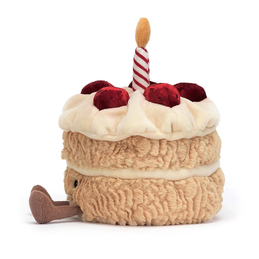 A side photo plush toy resembling a birthday cake with two layers, decorated with a red and white striped candle on top, and sliced pieces on the side.