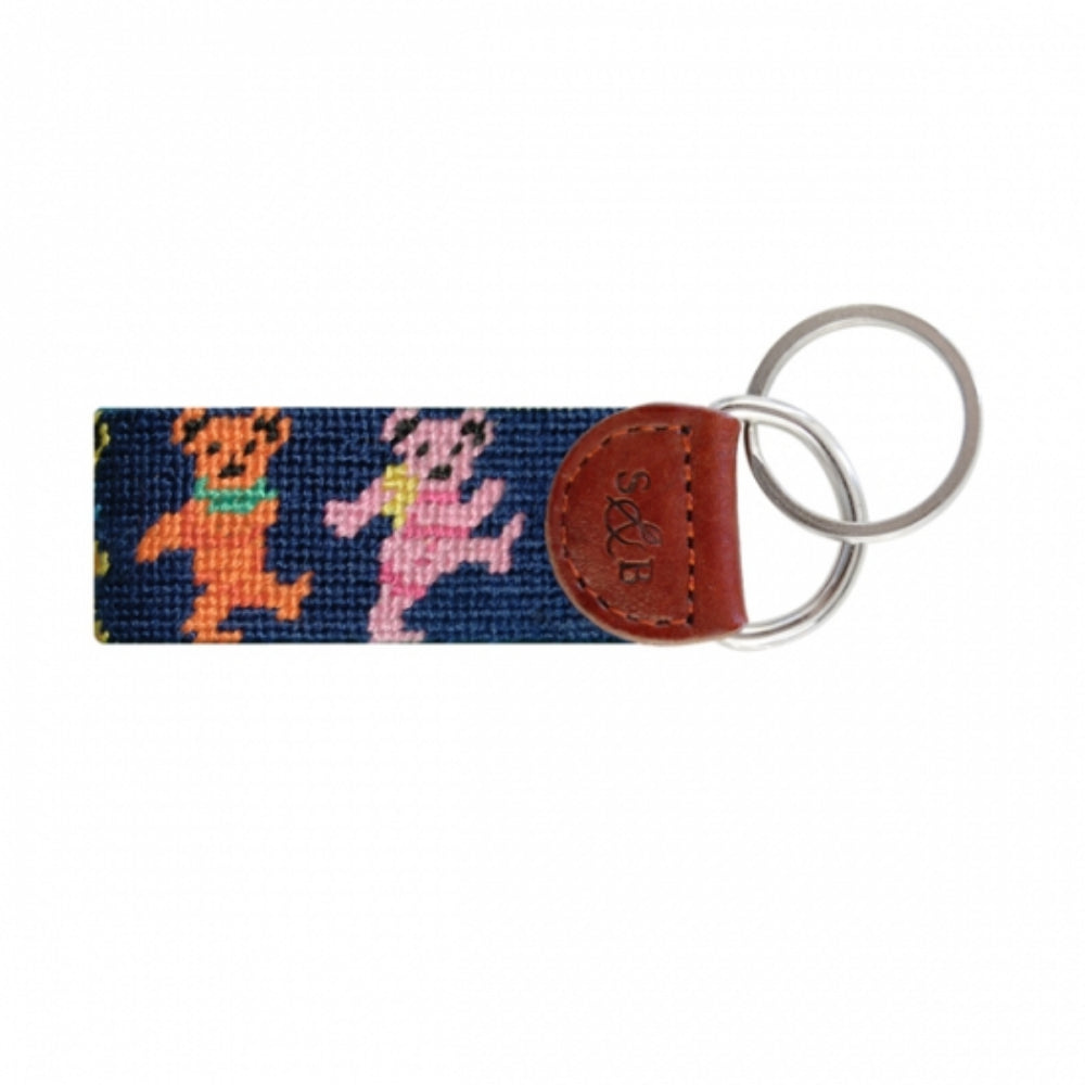 A needlepoint key fob featuring a colorful design of dancing bears attached to a key ring with a leather strap.