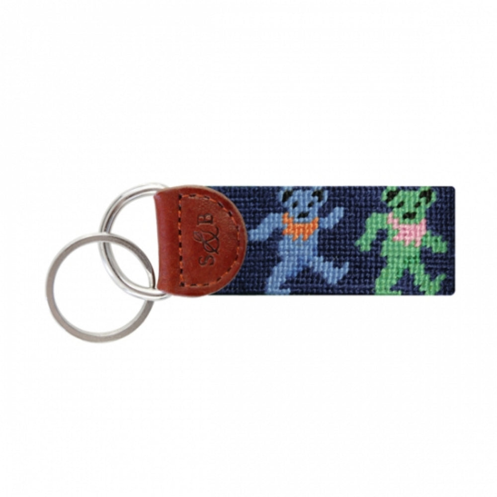 A needlepoint key fob featuring a colorful design of dancing bears attached to a key ring with a leather strap.