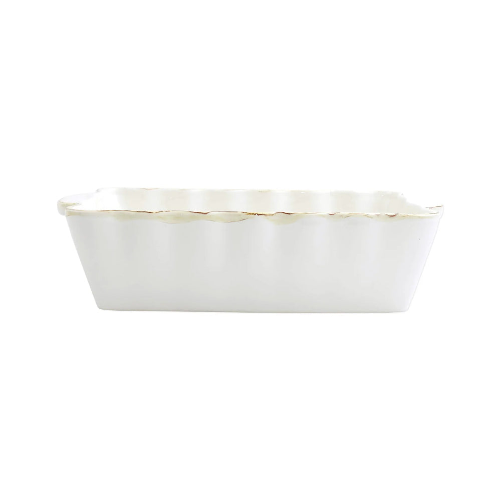 A medium white rectangular stoneware baker with scalloped edges and gold rim with a white interior